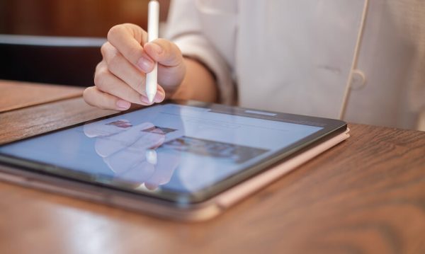 A person uses a stylus to interact with a tablet displaying a website, while seated at a wooden table.