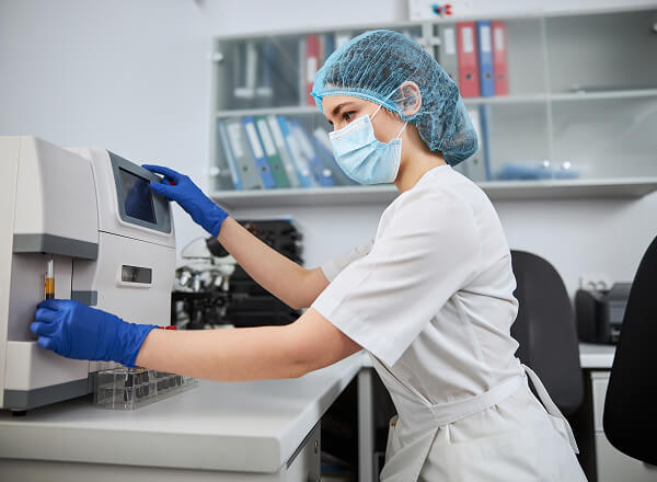 A lab technician in protective gear operates a medical analyzer in a laboratory setting.
