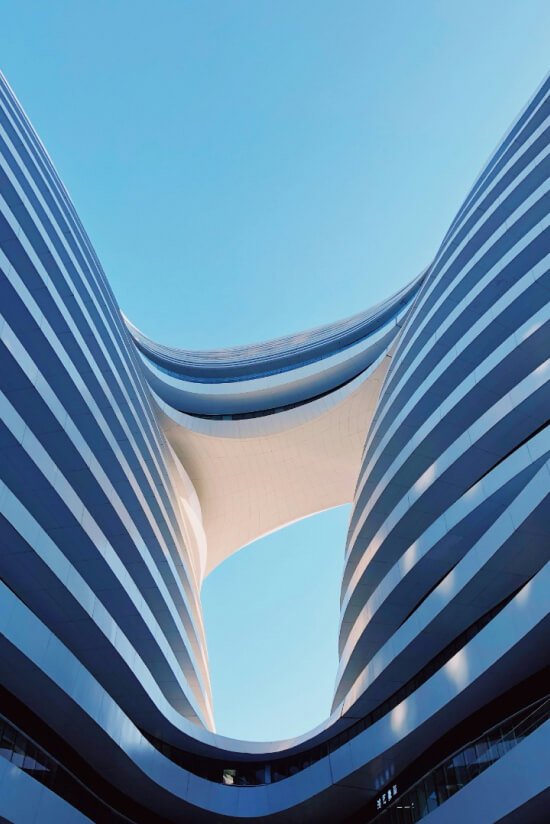 Two curved, white-striped buildings forming a unique archway against a clear blue sky.