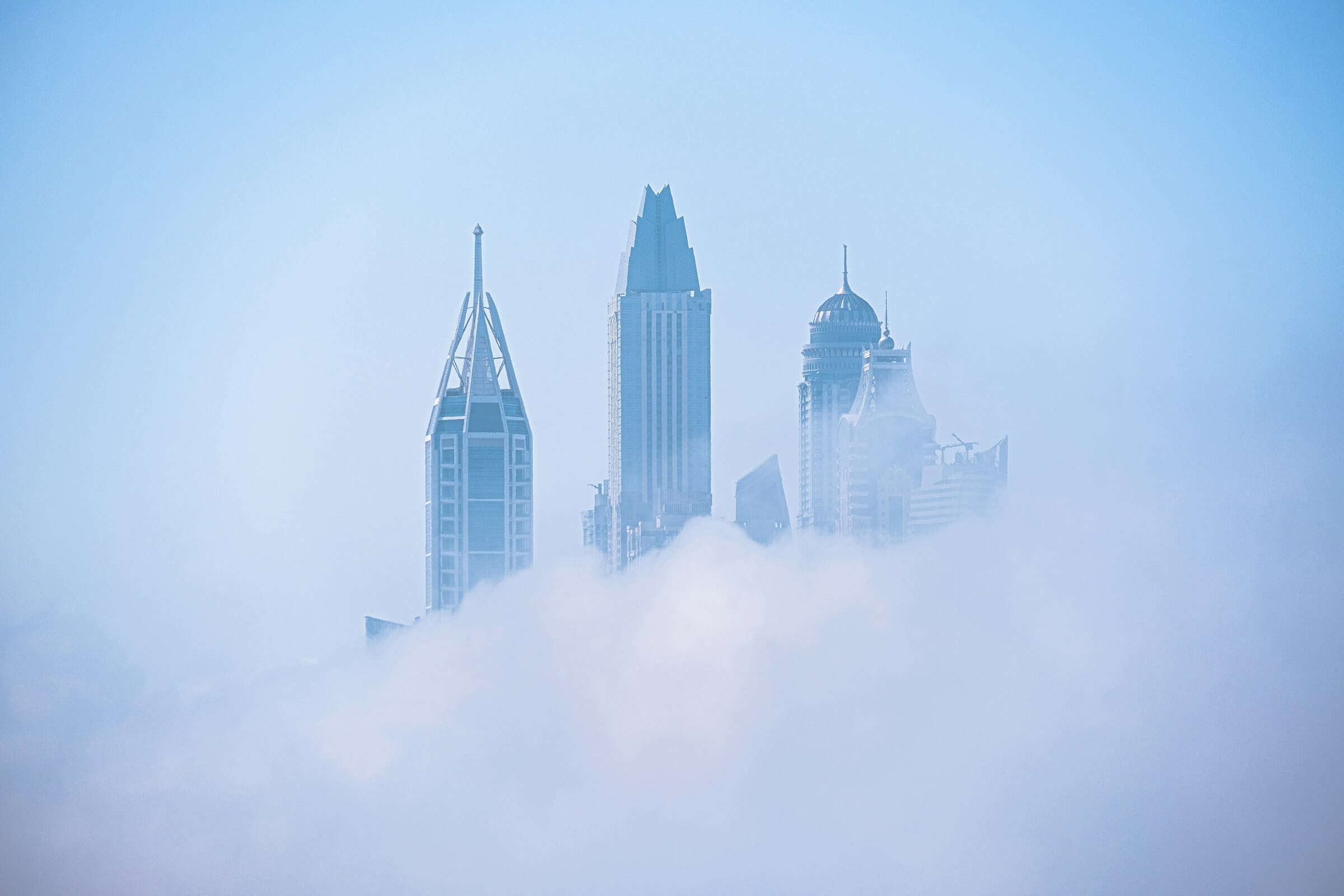 Skyscrapers peeking through dense fog against a clear sky.