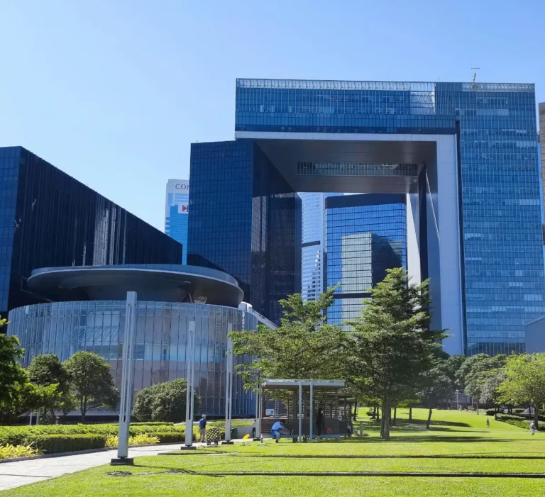 Modern cityscape featuring a large building with a distinctive square arch design, surrounded by greenery and a clear blue sky.