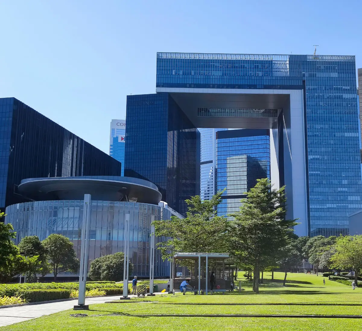 Modern cityscape featuring a large building with a distinctive square arch design, surrounded by greenery and a clear blue sky.