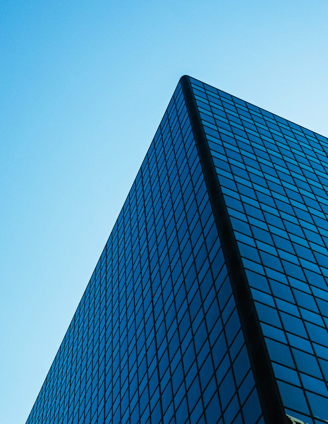Close-up view of a glass-paneled skyscraper against a clear blue sky, showcasing its geometric design and reflective windows.