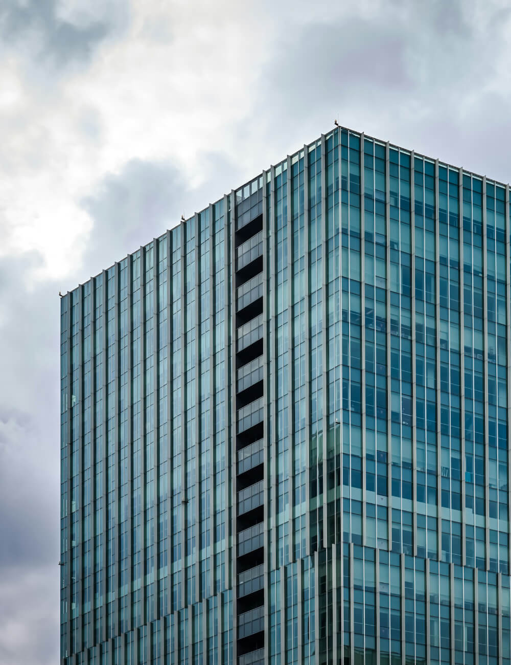 Glass-covered skyscraper corner against a cloudy sky.