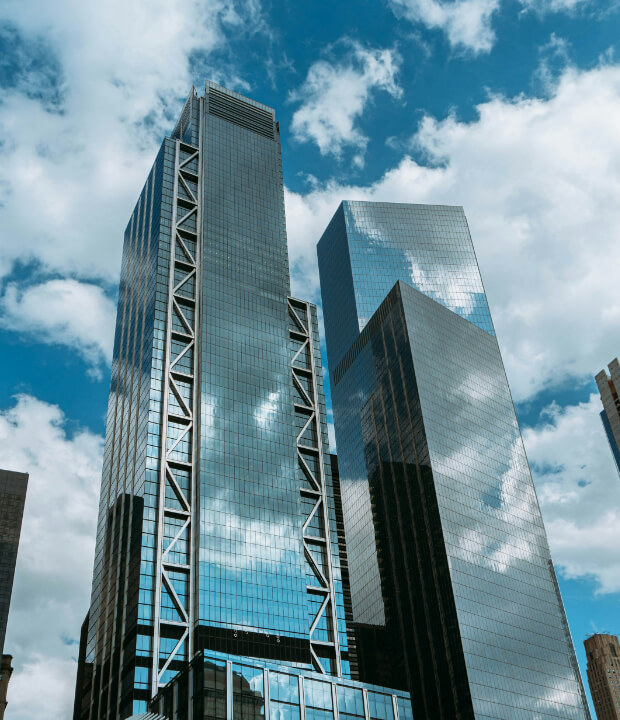Tall, modern glass skyscrapers reflect clouds under a blue sky.