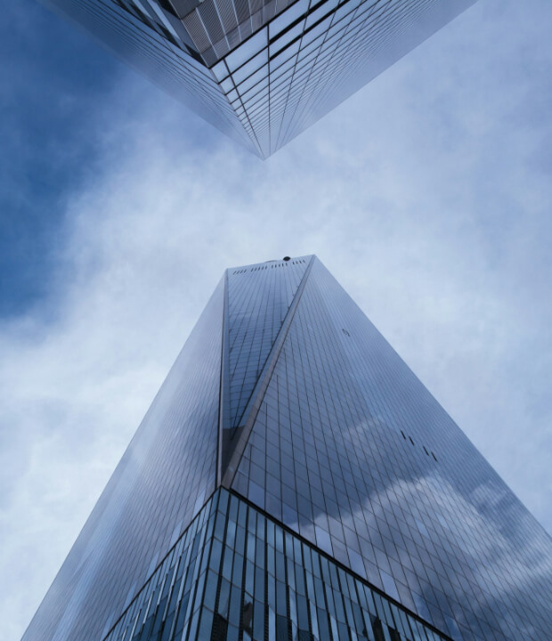 Looking up at two intersecting skyscrapers with reflective glass facades against a cloudy sky.