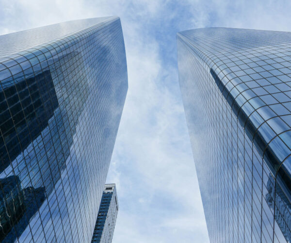 View of two tall glass skyscrapers against a cloudy sky.