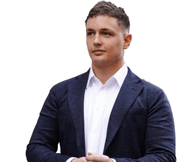 Kyle Hunt is wearing a white shirt and a blue suit jacket. He is standing with his hands clasped in front of him.