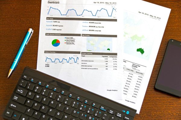 A printed Google Analytics report with charts and graphs lies on a desk next to a keyboard, pen, and smartphone.